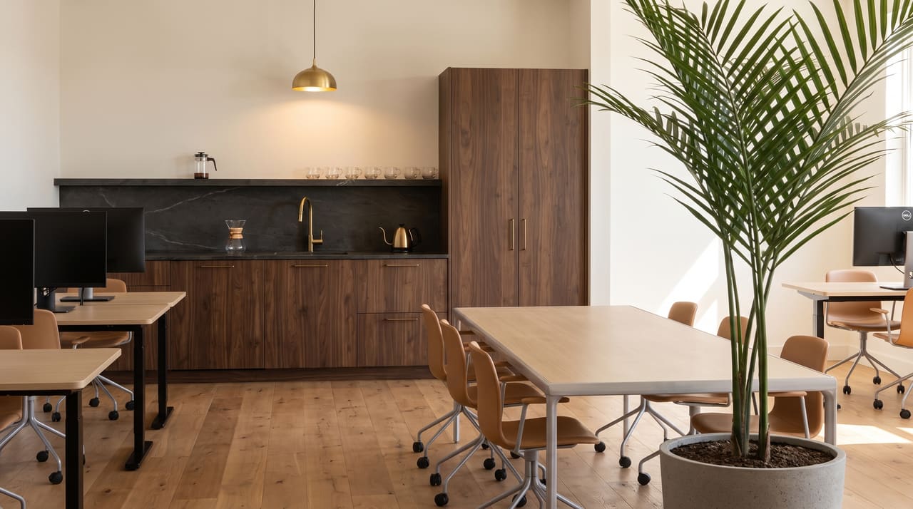 The self-serve hospitality corner: pour-over carafe, brass kettle and tea glasses on the dark stone counter, walnut cabinets, a brass tap and the tall walnut wardrobe beside.
